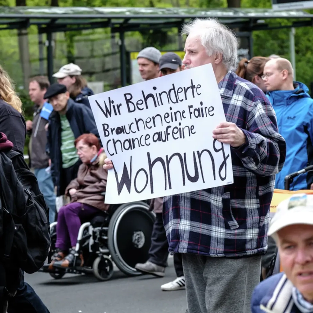 Ein Demonstrant auf der Straße hält ein Schild mit der Vorderung nach mehr behindertengerechten Wohnungen