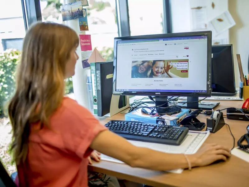 Eine Frau sitzt vor dem Computer. Auf dem Bildschirm ist die Starteseite des Aktion Mensch-Familienratgebers zu sehen.