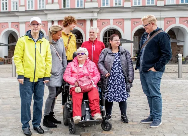 Eine Gruppe von Menschen mit und ohne Behinderung stehen auf einem Platz und unterhalten sich