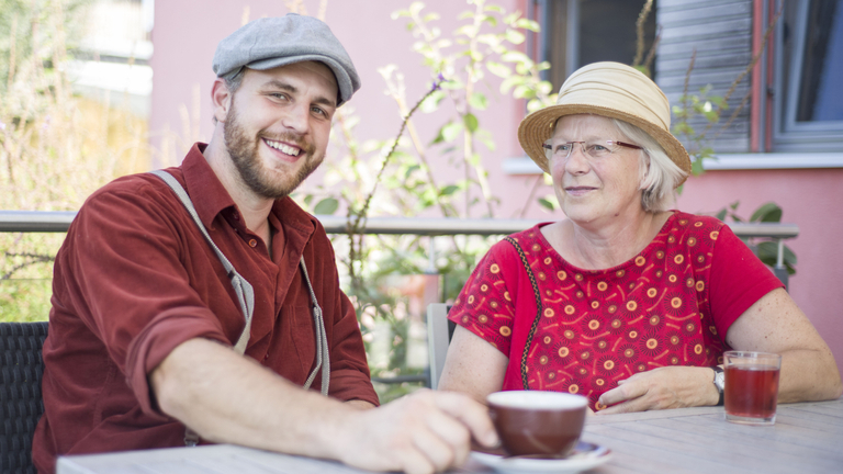 Ein junger Mann und eine ältere Frau sitzen draußen und trinken Tee.