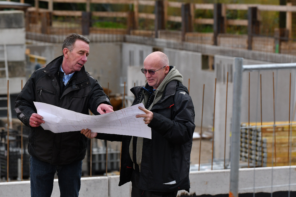 Zwei Männer stehen auf einer Baustelle und schauen gemeinsam in einen Plan.