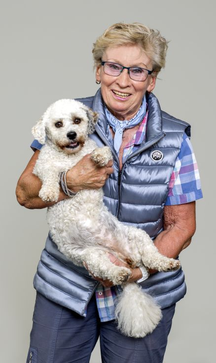 Eine ältere Frau hat einen Hund auf dem Arm und lächelt in die Kamera