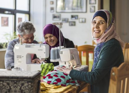Drei Frauen nähen an Nähmaschinen, zwei Frauen tragen ein Kopftuch.