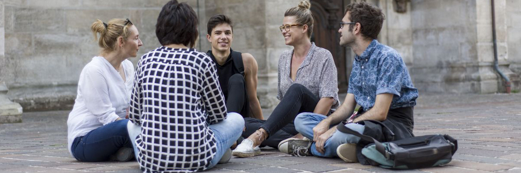 Eine Gruppe junger Menschen sitzt im Schneidersitz auf dem Vorplatz einer Kirche