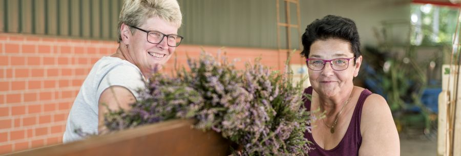 Zwei Frauen arbeiten an einen Gesteck für einen Festzug-Wagen, sie lächeln