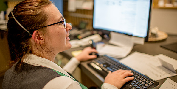 Eine Frau sitzt vor einem Computer. Ihre Hände liegen auf der Tastatur.