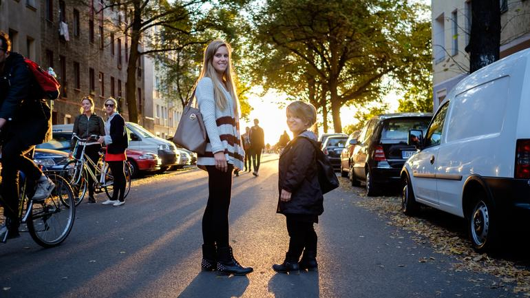 Nicole und Jacqueline stehen sich auf einer Straße gegenüber und lächeln in die Kamera. Im Hintergrund sieht man die untergehende Sonne.