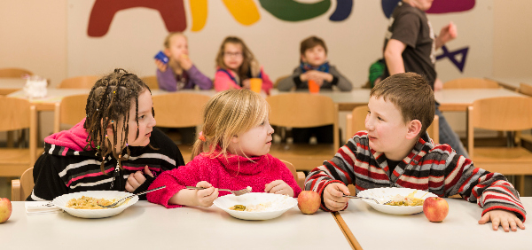 Drei Kinder sitzen zusammen und essen.