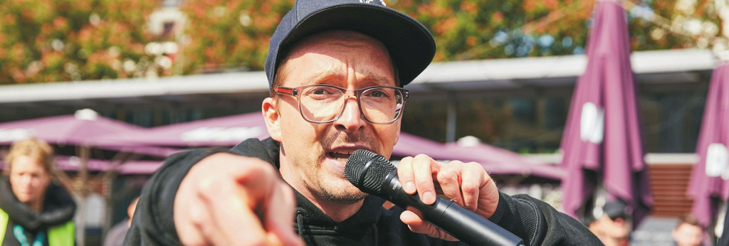 Ein Sänger ruft ins Mikrofon und zeigt in die Kamera.
