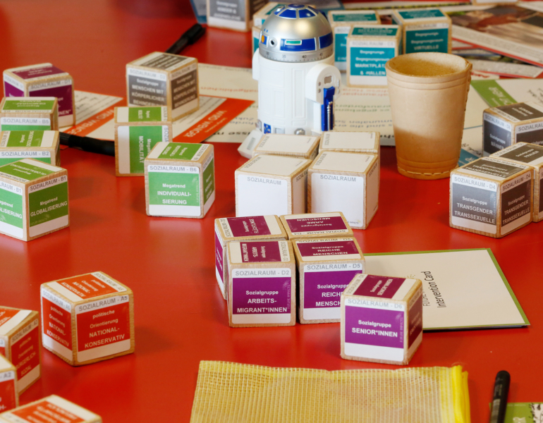 Bei einem Workshop liegen verschiedene Spielutensilien auf einem roten Tisch.