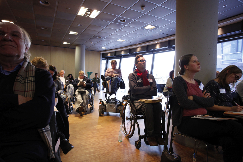 Die Teilnehmer hören gespannt zu und machen sich Notizen. Darunter sind 3 Rollstuhlfahrer.