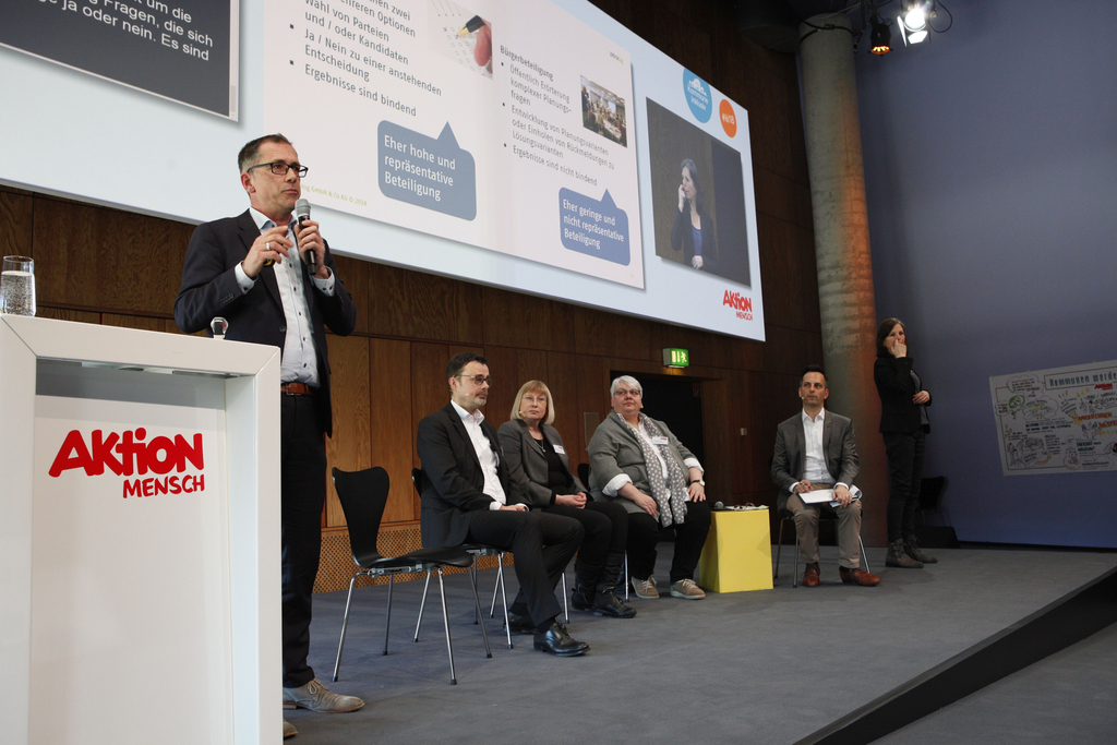 Auf der Bühne steht Oliver Märker bei seinem Vortrag. Prof. Dr. Peter Neumann, Doris Rüter, Dr. Bettina Kruth und der Moderator Frank Liffers sitzen auf der Bühne