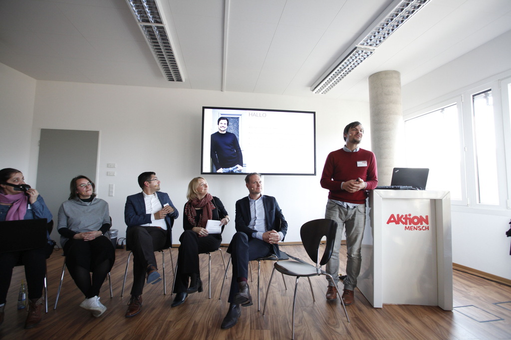 Michael Vollmann steht am Pult und hält seinen Vortrag. Diverse Gäste sitzen neben ihm.