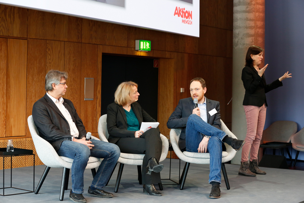 Auf der Bühne: Die Moderatorin Katja Nellissen im Gespräch mit Prof. Dr. Dieter Katzenbach und Dr. Hendrik Trescher. Eine Gebärdensprachdolmetscherin übersetzt