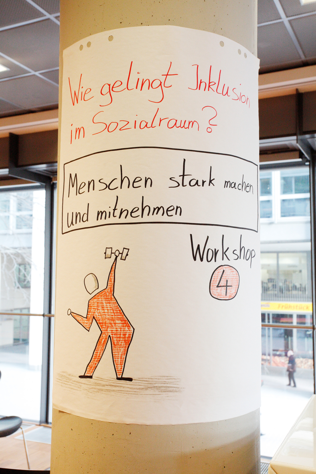 An einem Pfeiler hängt eine Zeichnung mit der Bezeichnung des Workshops