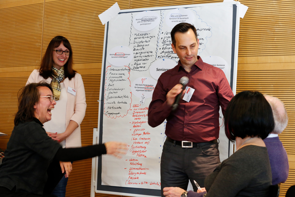 Der Referent Frank Liffers steht mit einem Mikrofon vor einem selbstgestaltetem Plakat. 