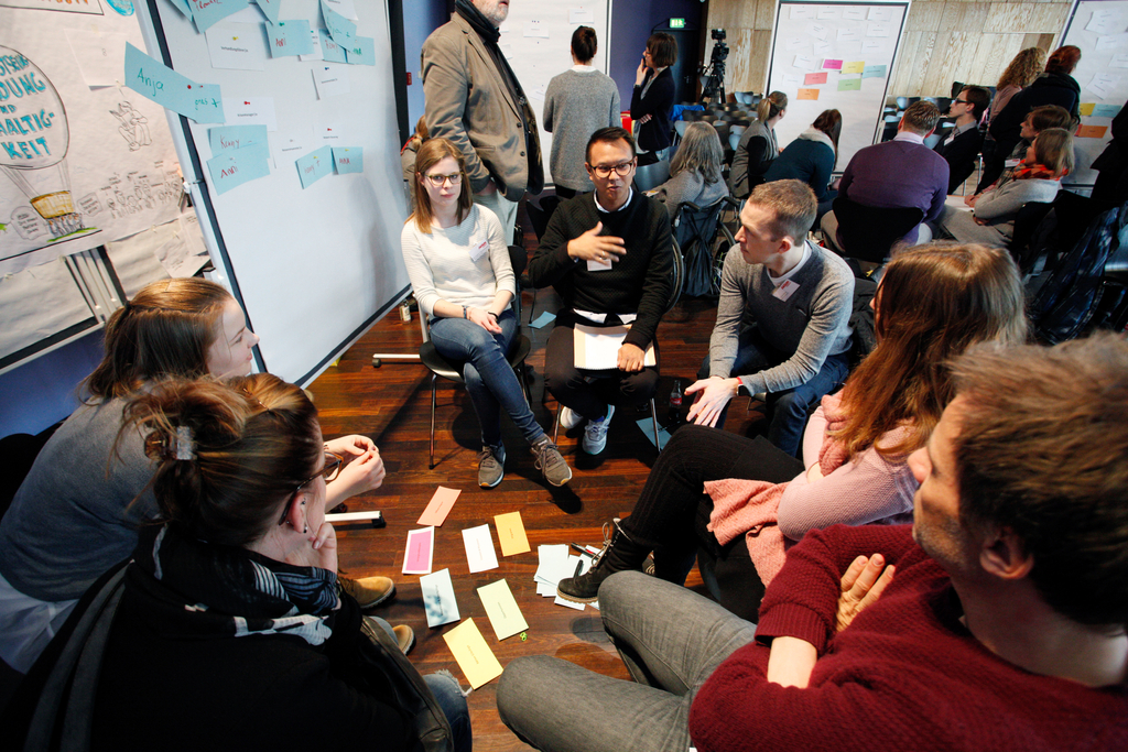 Teilnehmer in einem Gesprächskreis. Auf dem Boden vor ihnen liegen bunte Pappkarten