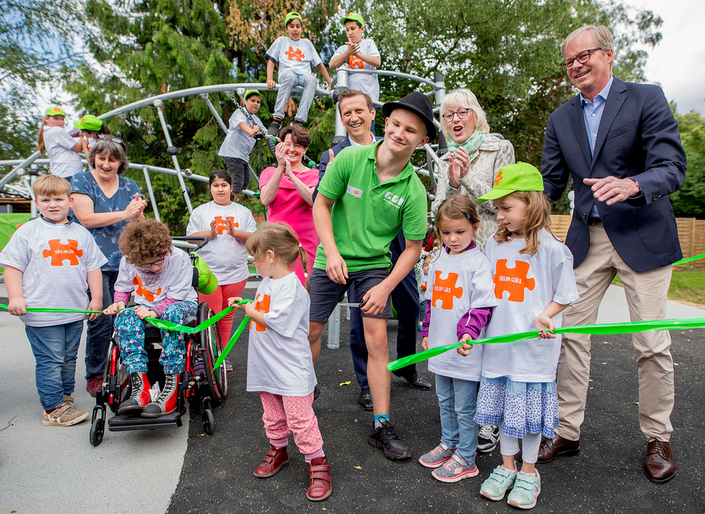 Kinder mit und ohne Behinderungen und Erwachsene stehen vor einem Kletterspielgerät und lachen in die Kamera.