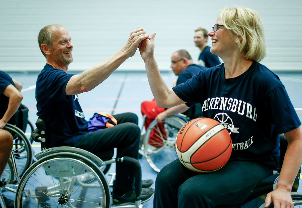 Zwei Rollstuhlbasketballer klatschen sich mit den Händen ab.
