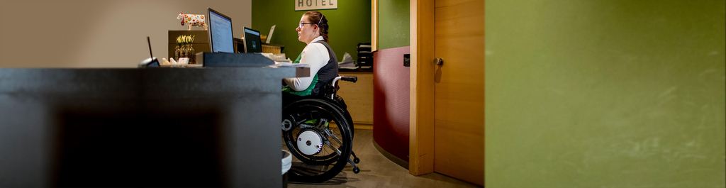Eine Frau im Rollstuhl arbeitet an der Rezeption eines Hotels.