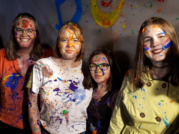 Vier mit Farbkleksen bunt besprenkelte junge Frauen.