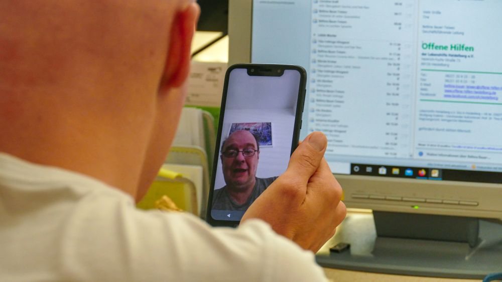 Ein Mann hält ein Smartphone in der Hand und führt einen Videochat mit einem anderen Mann.