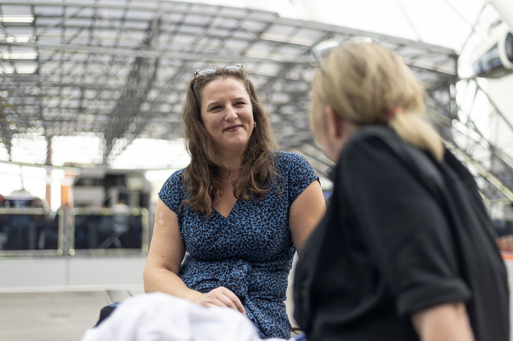 Zwei Frauen sitzen sich gegenüber und sprechen miteinander. Eine der Frauen sieht man nur von hinten, die andere schaut in Richtung der Kamera.
