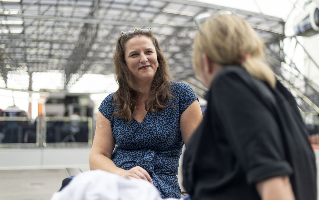 Zwei Frauen sitzen sich gegenüber und sprechen miteinander. Eine der Frauen sieht man nur von hinten, die andere schaut in Richtung der Kamera.