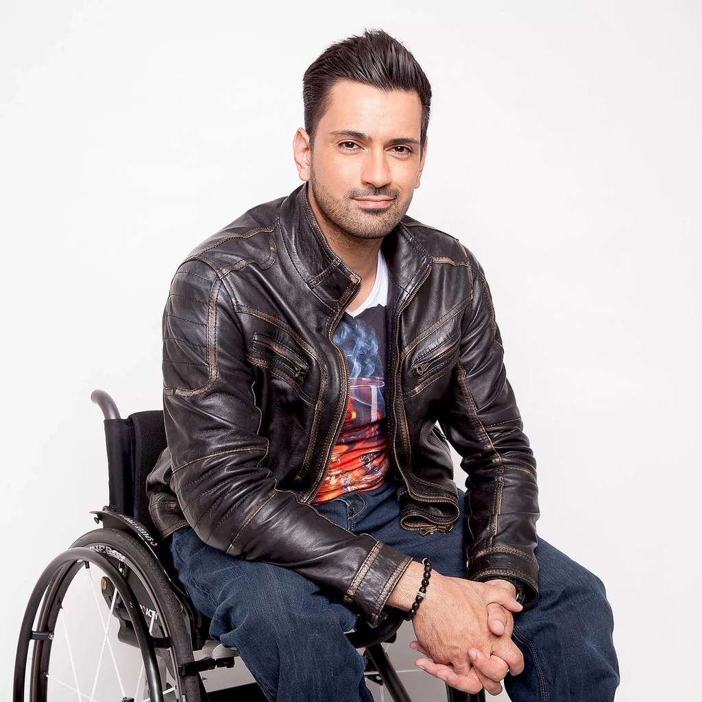 Ein Mann mit schwarzen kurzen Haaren und Lederjacke sitzt lässig in einem Rollstuhl.