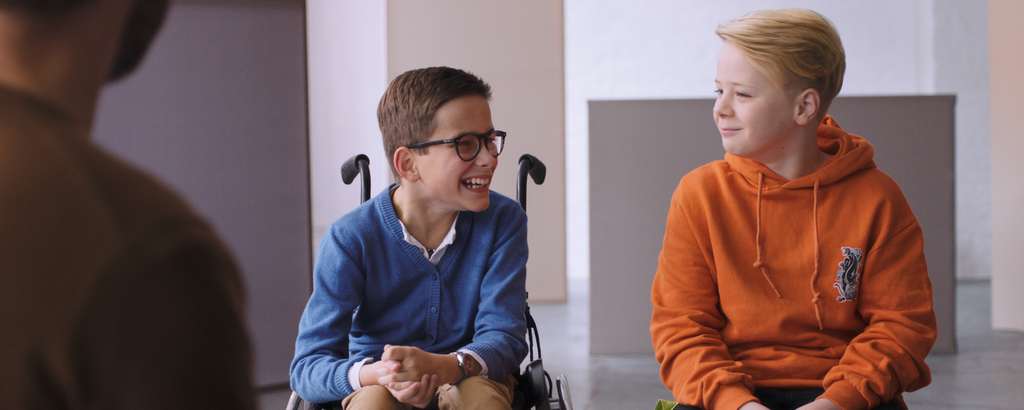 Zwei Jungen, einer davon im Rollstuhl, lachen gemeinsam.