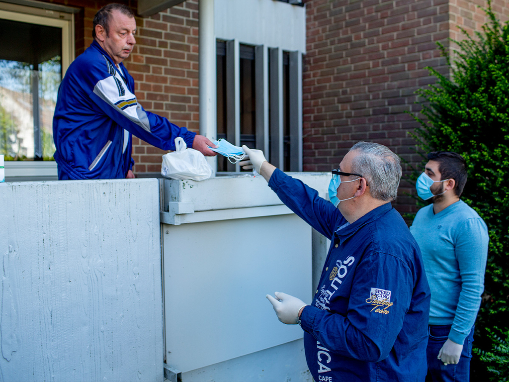 Zwei Männer verteilen Mundschutzmasken über den Balkon an einen anderen Mann.