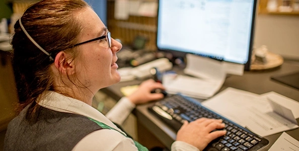 Eine Frau sitzt vor einem Computer. Ihre Hände liegen auf der Tastatur.
