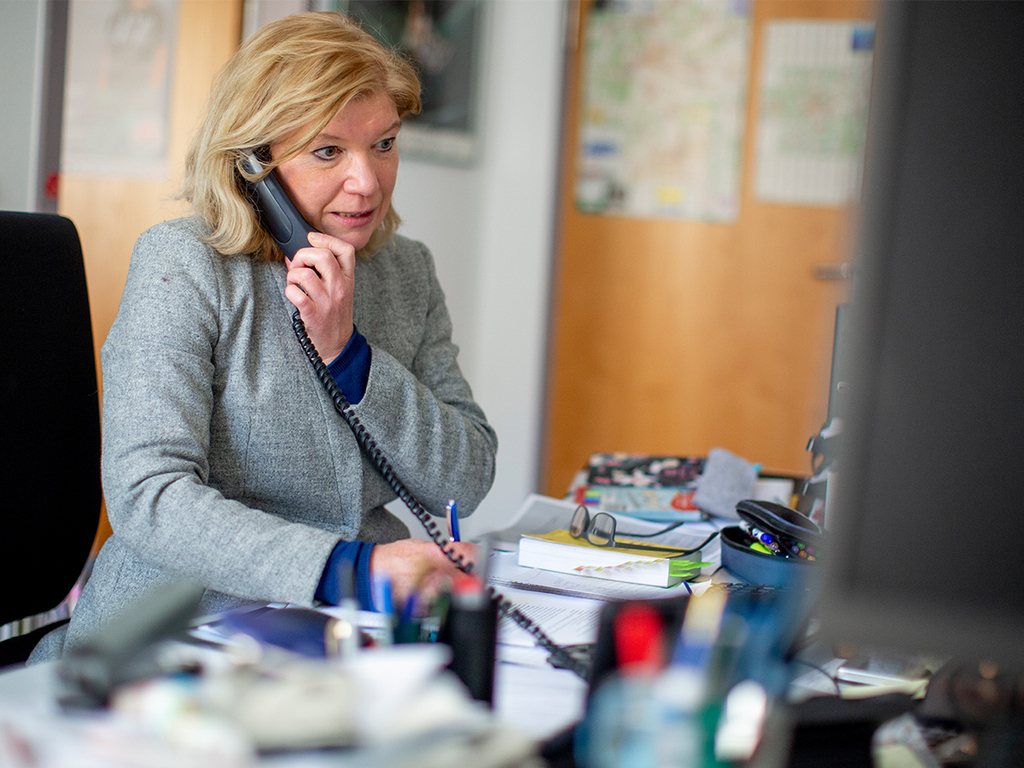 Ein Frau sitzt am Arbeitspaltz und telefoniert.