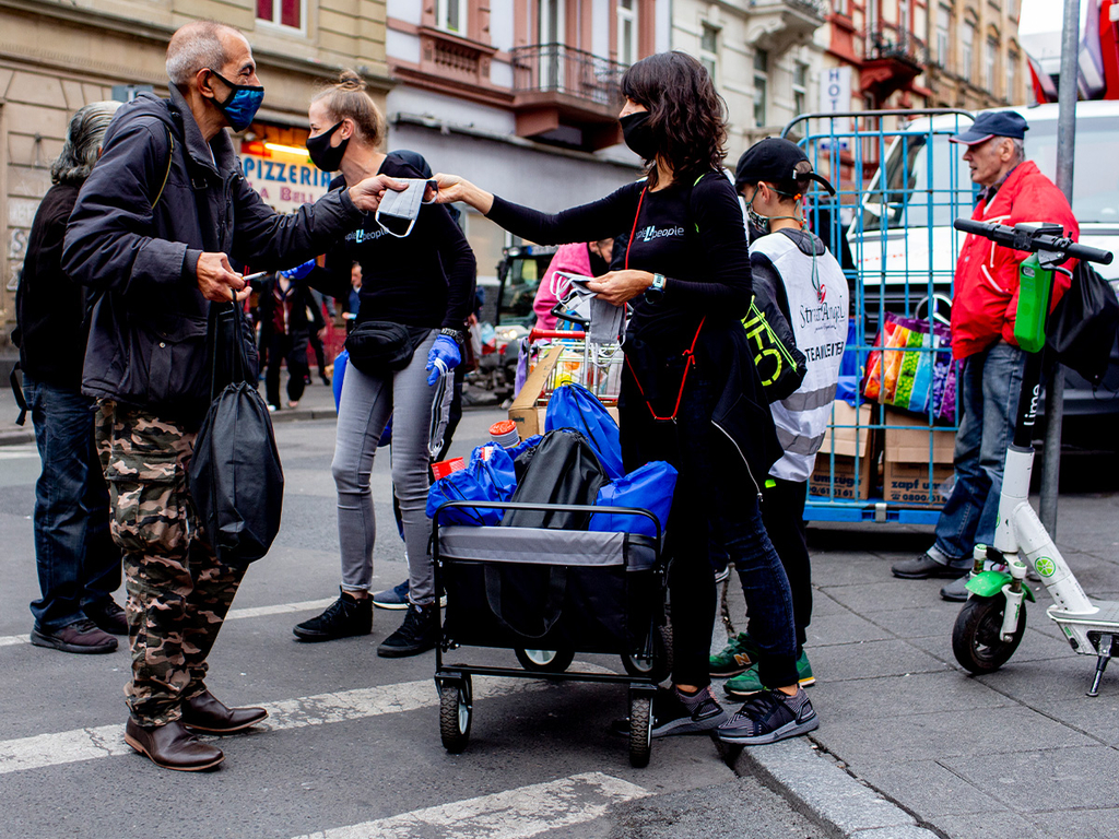 Zwei Frauen und ein Junge verteilen gepackte Tüten an Obdachlose.