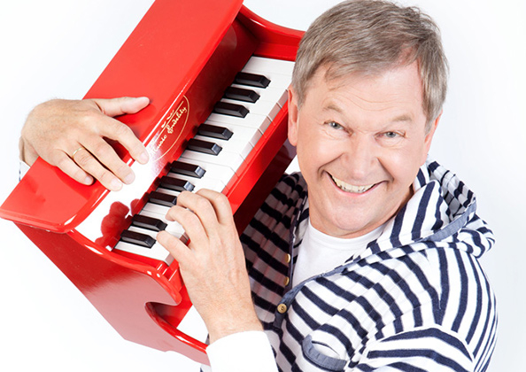 Reinhard Horn mit einem roten, kleinem Klavier in den Händen.