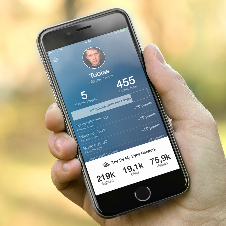 Hand, die ein Handy hält, im Display die Be My Eyes App