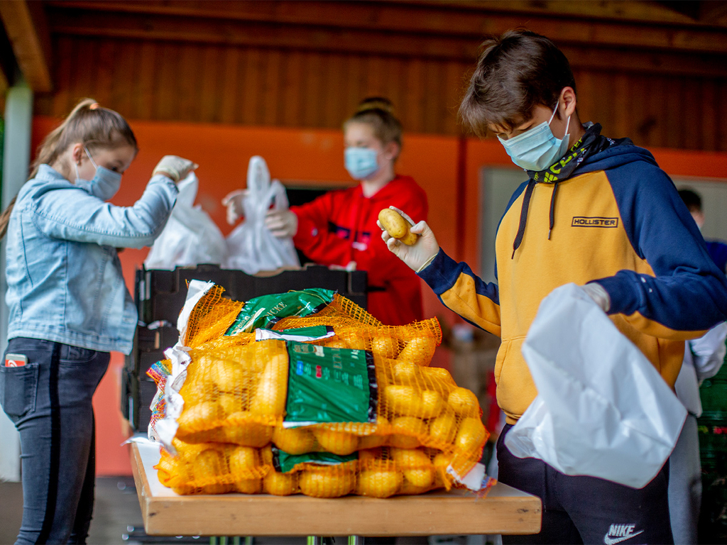 Drei Jugendliche mit Mundschutz verpacken Kartoffeln.