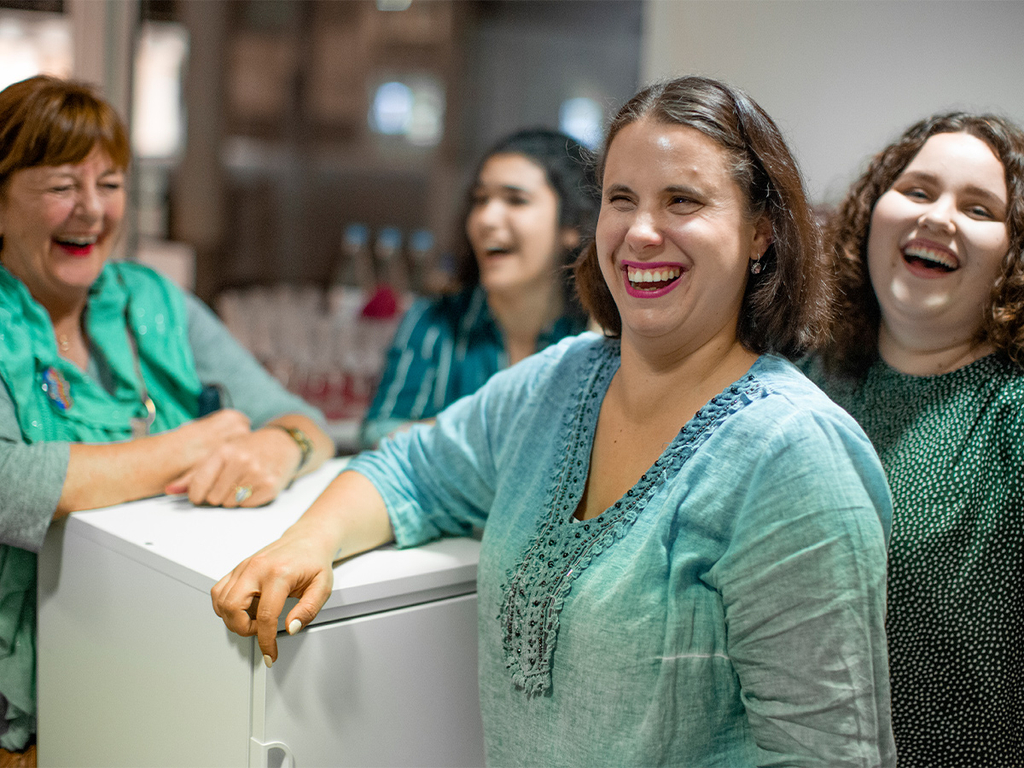 Vier Frauen stehen zusammen und lachen.