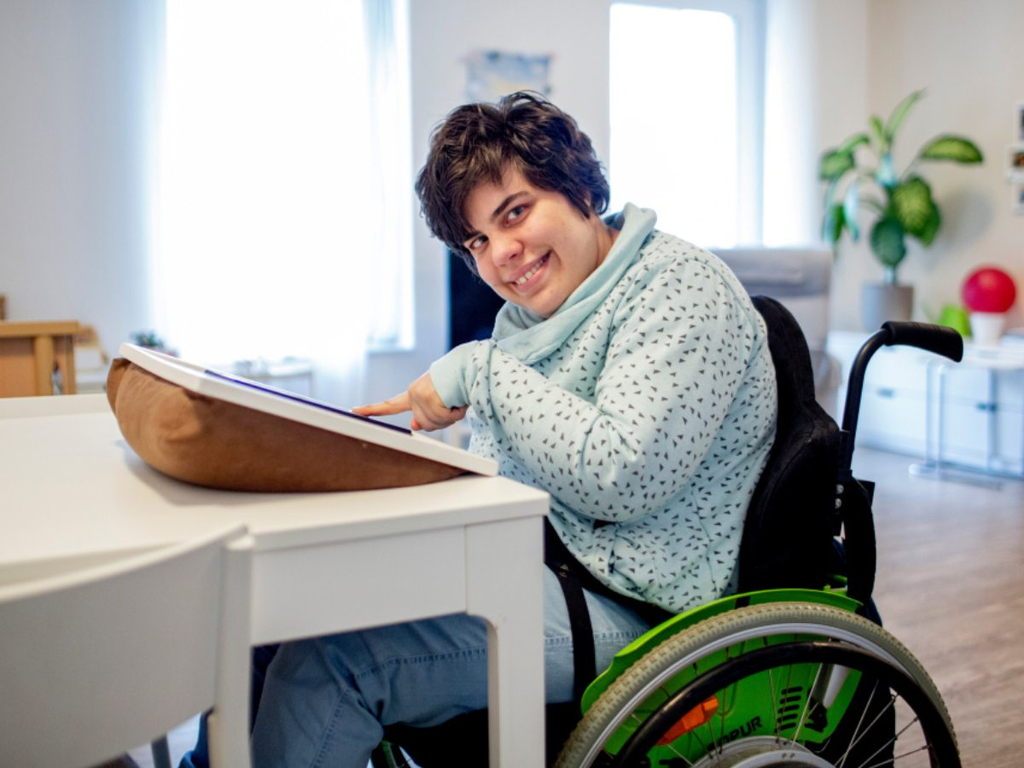 Eine Frau im Rollstuhl arbeitet an einem Tisch an einem Tablet.