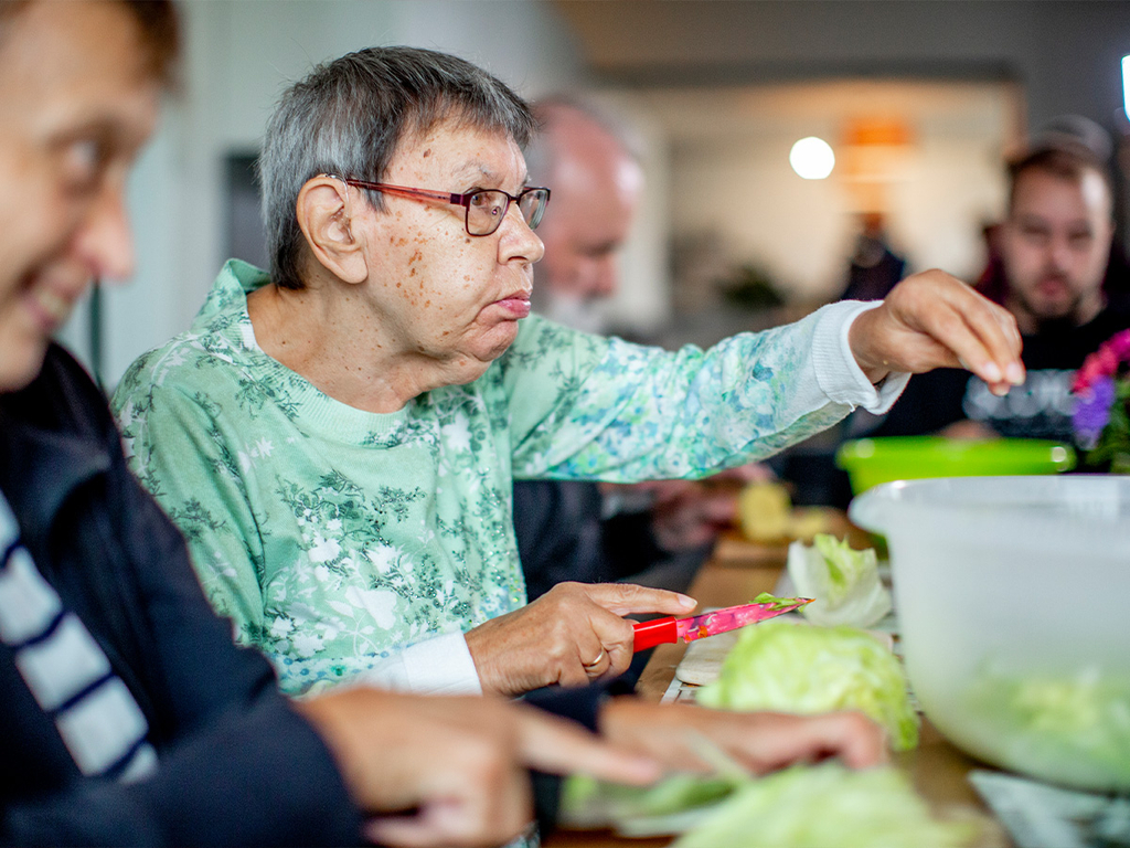 Eine Frau sitzt am Tisch und schneidet Salat.