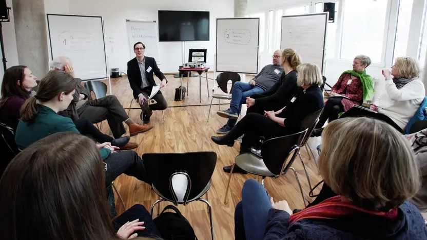 Ein Mann spricht vor eine Gruppe von Menschen, die im Halbkreis sitzen.