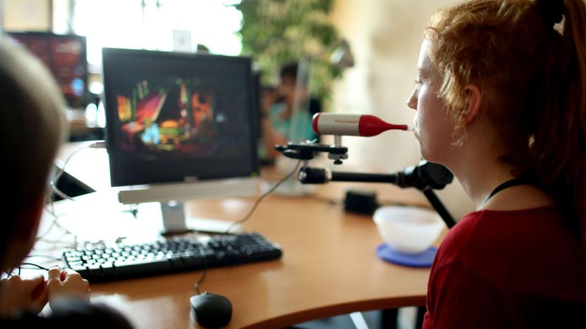 Eine junge Frau sitzt vor einem Bildschirm und nutzt eine Mundmaus. 