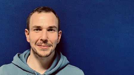 Fabio Priano, ein junger Mann mit kurzen braunen Haaren und Drietagebart.