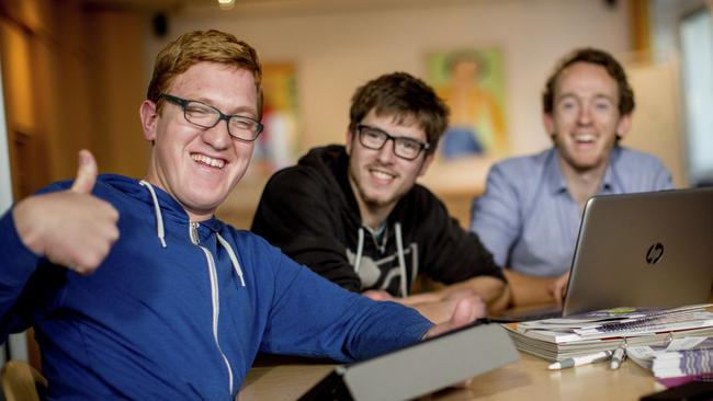 Drei Männer mit und ohne Behinderung sitzen an einem Schreibtisch vor zwei Laptops. Einer von ihnen gibt das Daumen-hoch-Zeichen. Alle drei lachen.