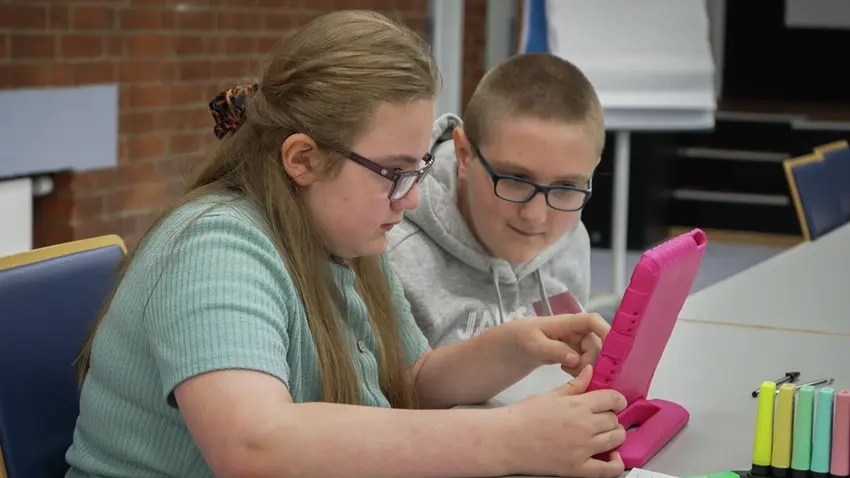 Zwei Jugendliche sitzen an einem Tisch und schauen gemeinsam auf ein Tablet.