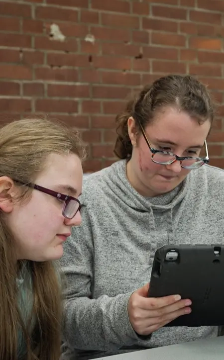Zwei Jugendliche und Bianca Rilinger sitzen nebeneinander auf einer Bank. Sie alle schauen auf ein Tablet, dass das Mädchen in der Mitte in der Hand hält.