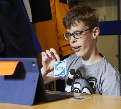 Ein Junge sitzt an einem Tisch vor einem iPad und hält eine Spielkarte in der Hand.