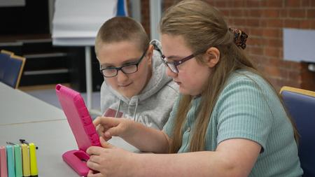 Zwei Jugendliche sitzen an einem Tisch und schauen gemeinsam auf ein Tablet.