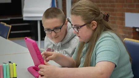 Zwei Jugendliche sitzen an einem Tisch und schauen gemeinsam auf ein Tablet.