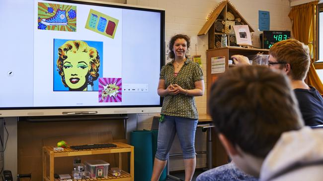 Eine Lehrerin steht vor einem Smartboard. Zwei Schüler schauen zu ihr hin.